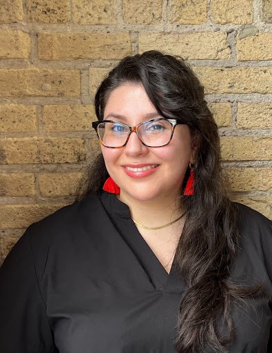 Libby Ebert is a mixed race, light-skinned woman with black hair, glasses, and red earrings. 